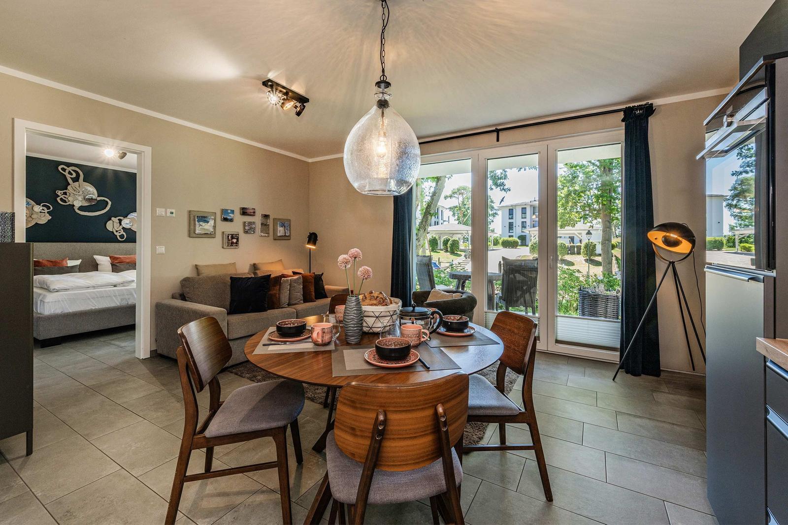 Essbereich mit Tisch und Stühlen, Wohnbereich mit Sofa und Schlafzimmer im Hintergrund.