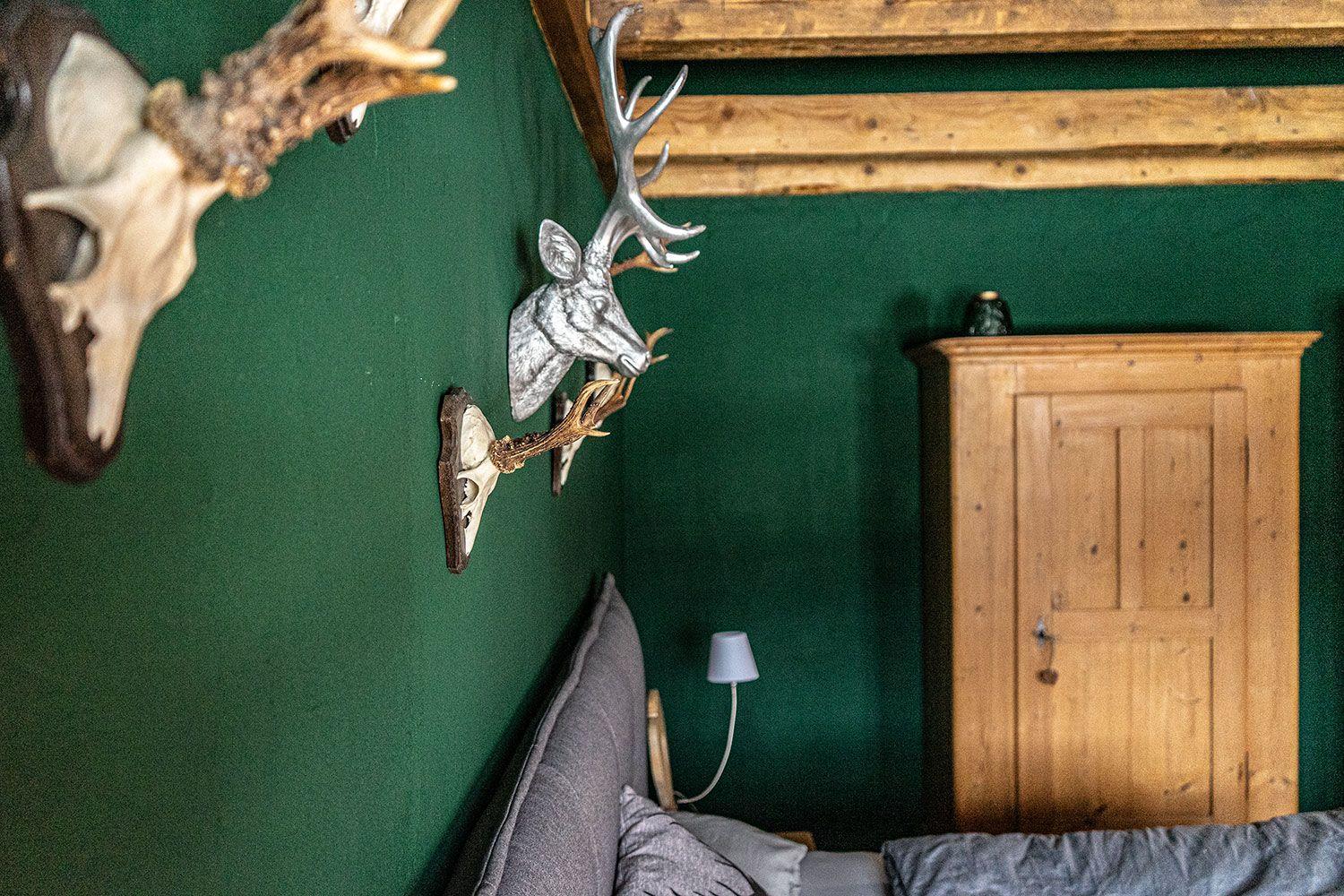 Bedroom with green wall, wooden beams, wardrobe, and wall decor with deer antlers.