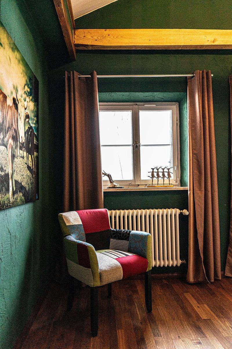 A room with green walls, a colorful chair, and a window with curtains.