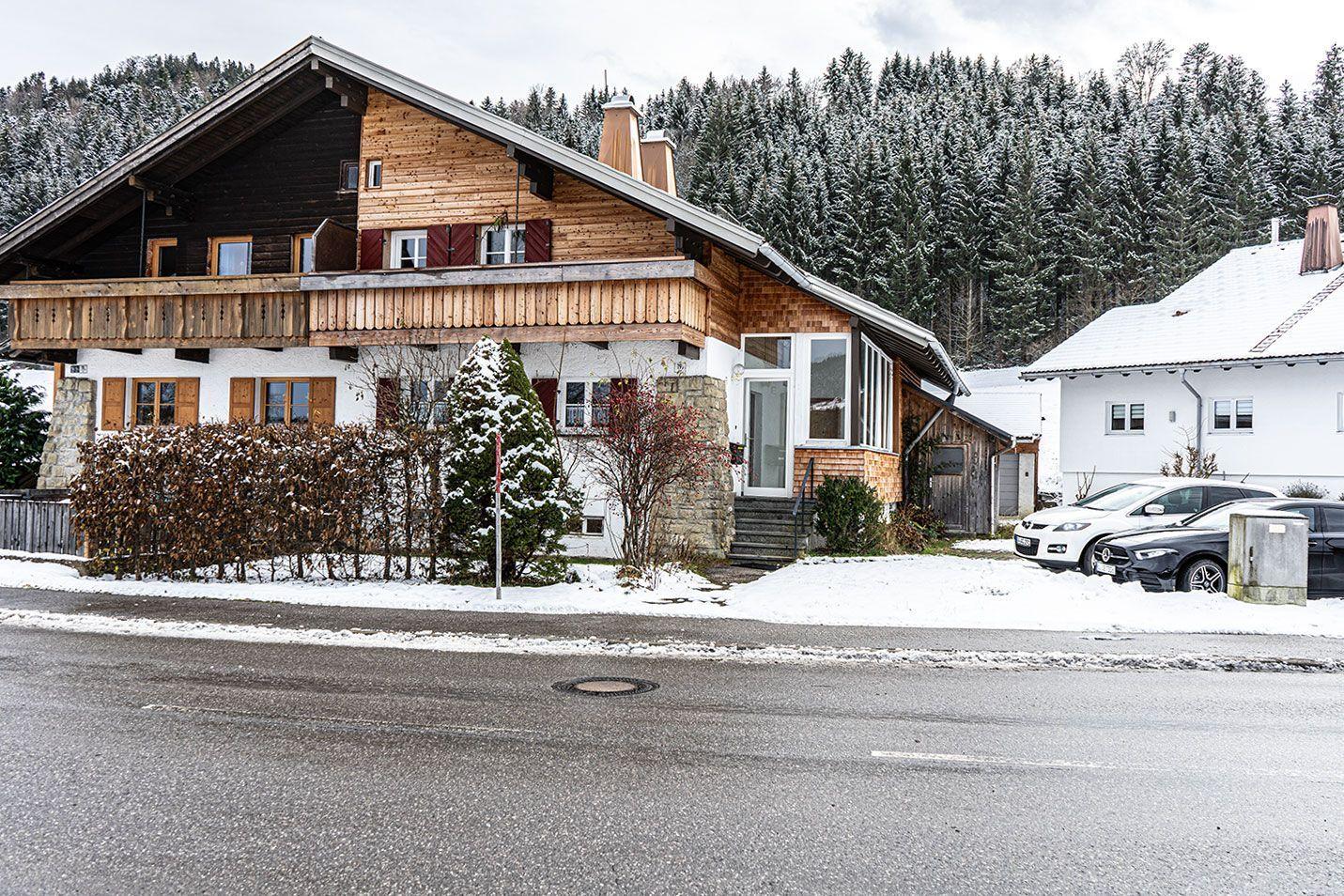 Wooden house with balcony, snow, and forest in the background.