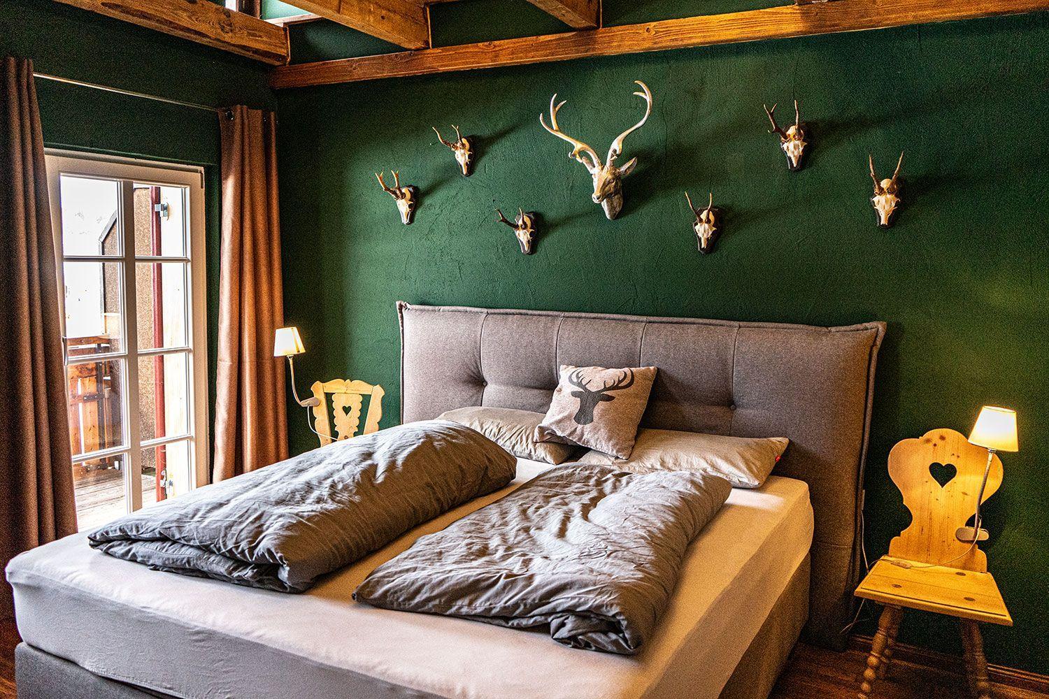Bedroom with green wall, wooden beams, and deer heads on the wall.