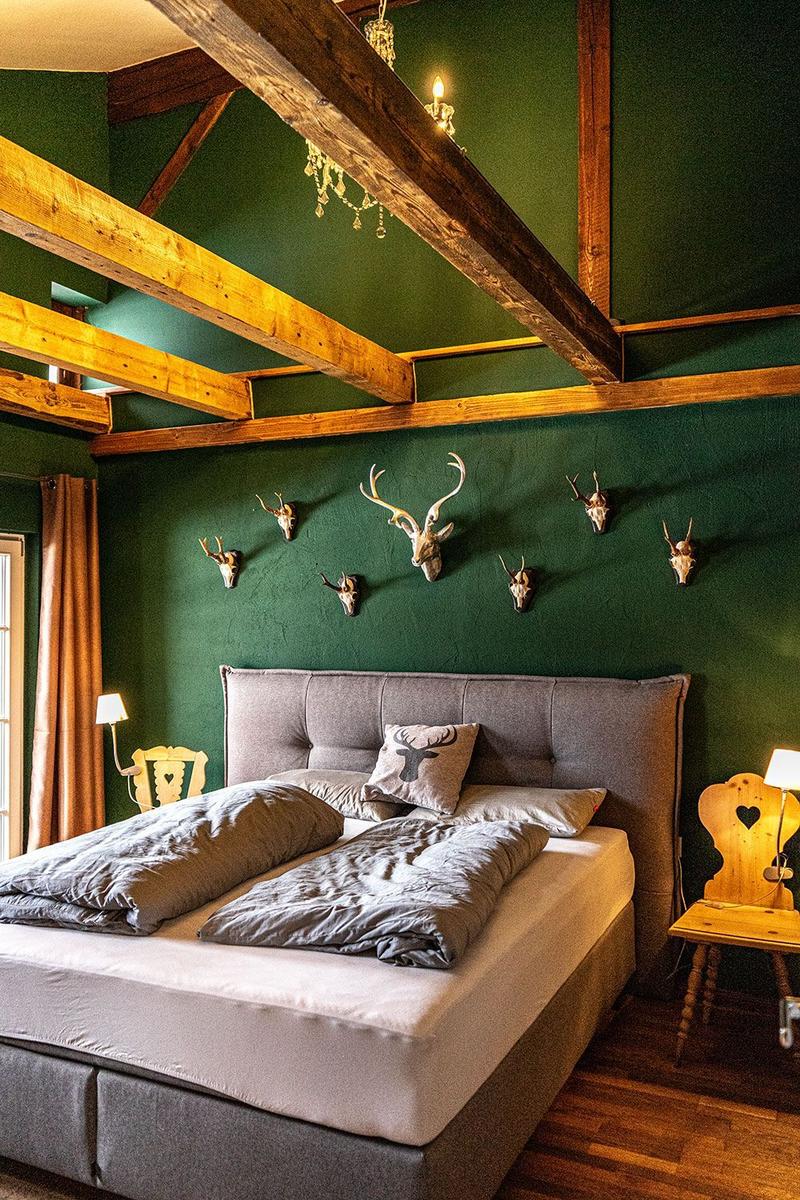 Bedroom with green wall, wooden beams, and deer heads on the wall.