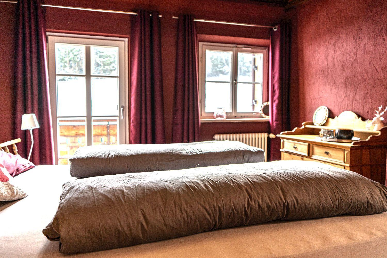 Bedroom with two beds, red walls, and windows with curtains.