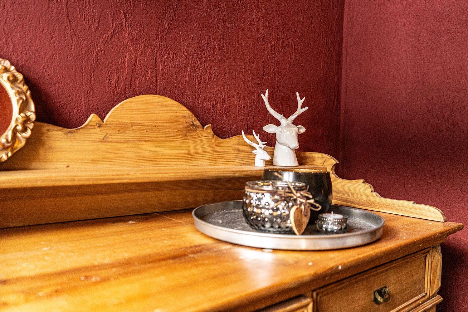 Wooden dresser with silver trays and white deer figures against red wall.