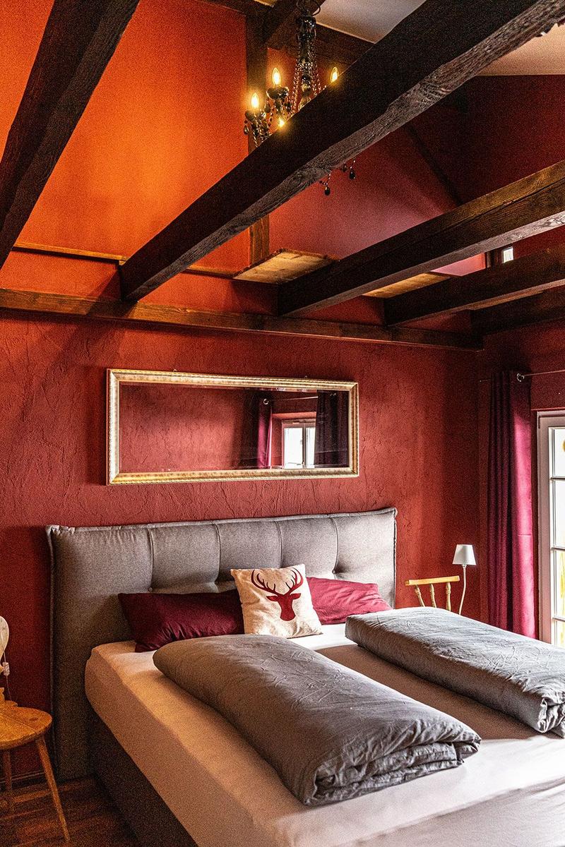 Bedroom with bed, wall mirror, and wooden beam ceiling. Red walls and curtains.