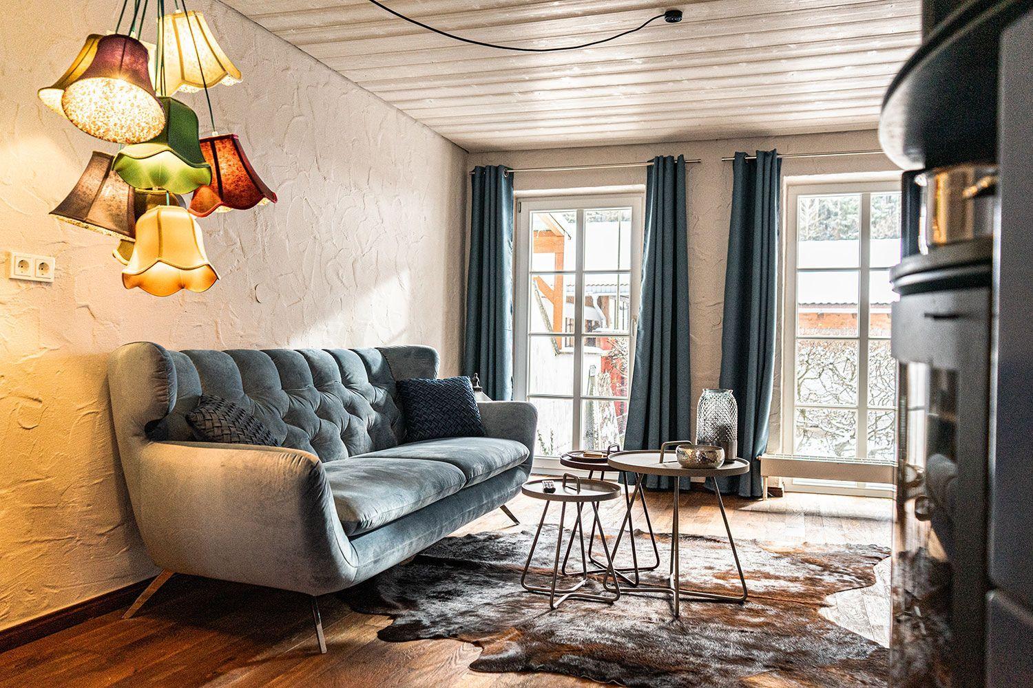 A living room with a sofa, tables, and windows with curtains.