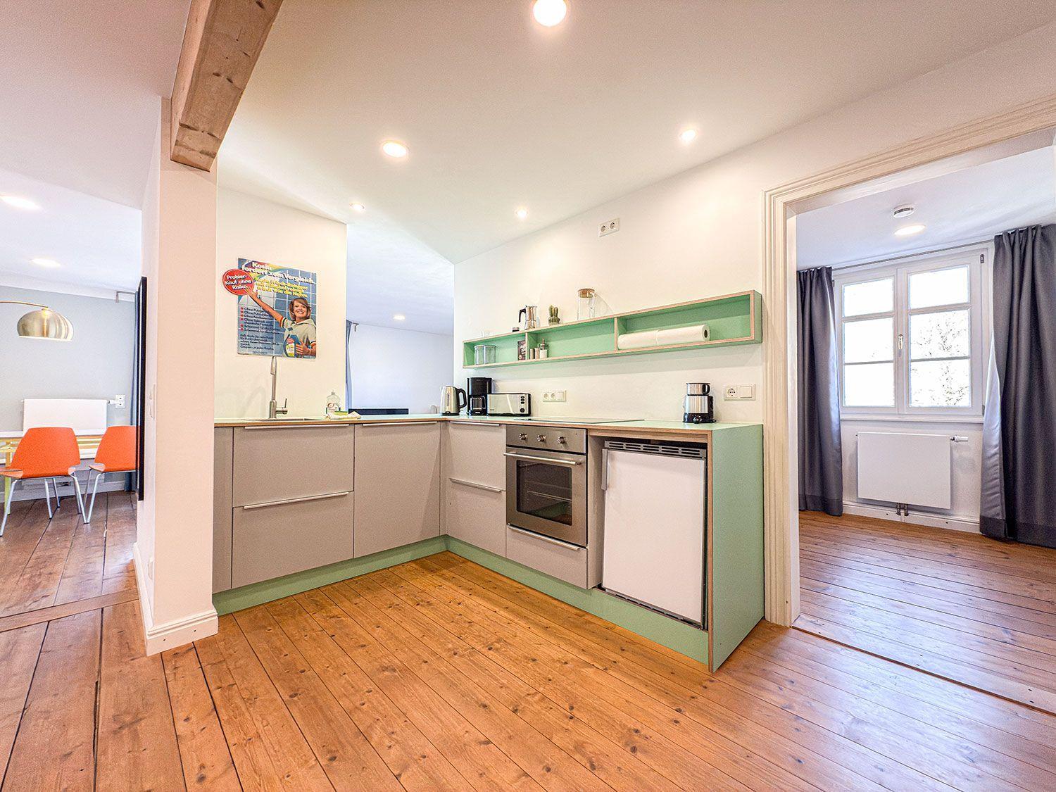 Kitchen with wooden floor, green accents, and built-in appliances.