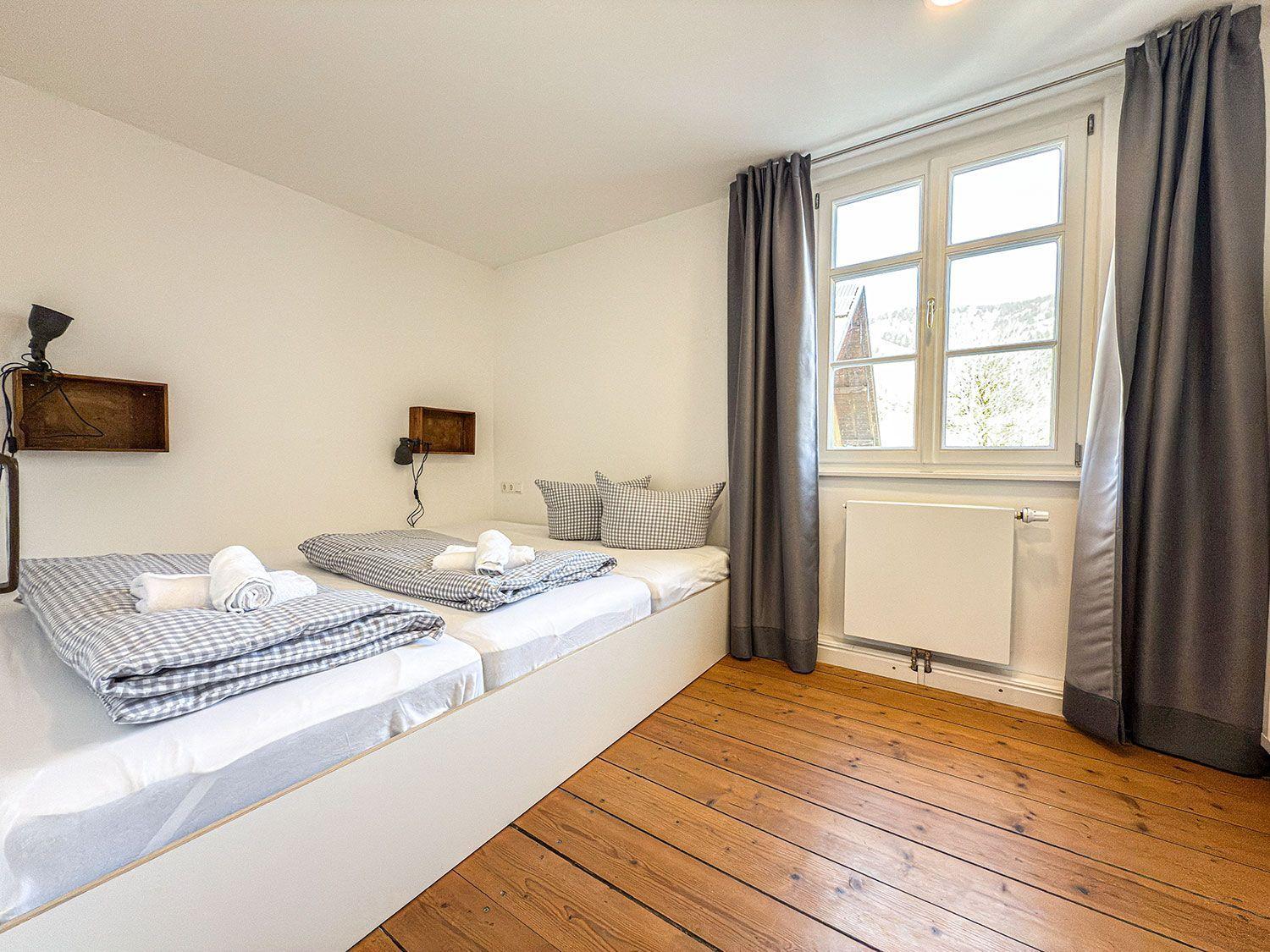 Room with two beds, wooden floor, and window with view of surroundings.