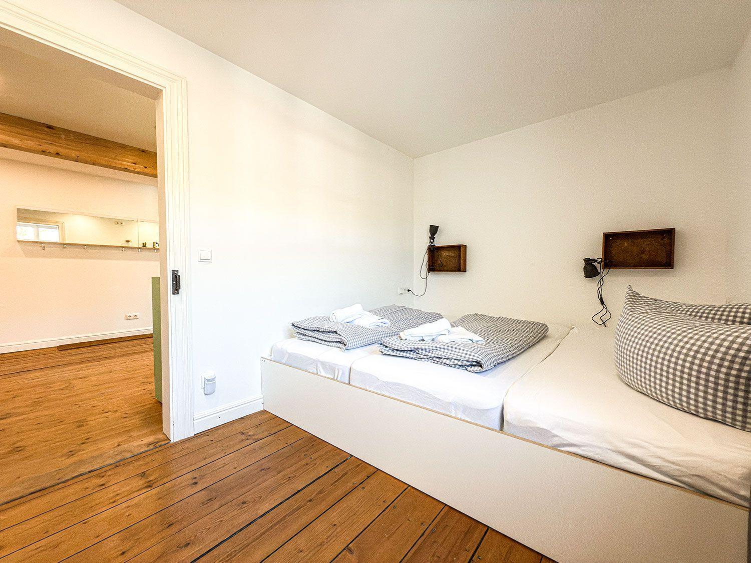 Bedroom with double bed, wooden floor, and view into adjacent room.