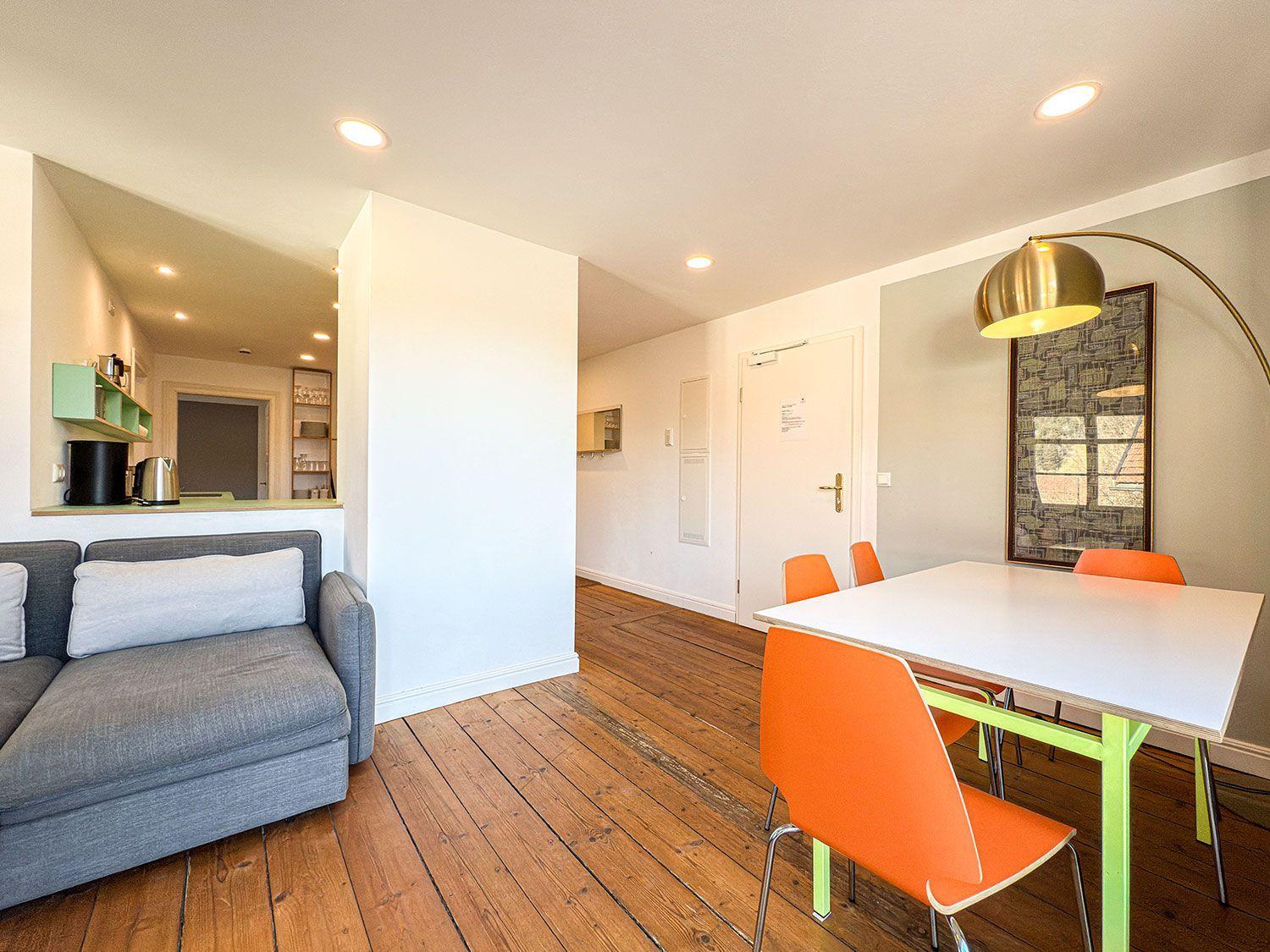 Apartment with dining area, sofa, and wooden floor. Table with orange chairs.