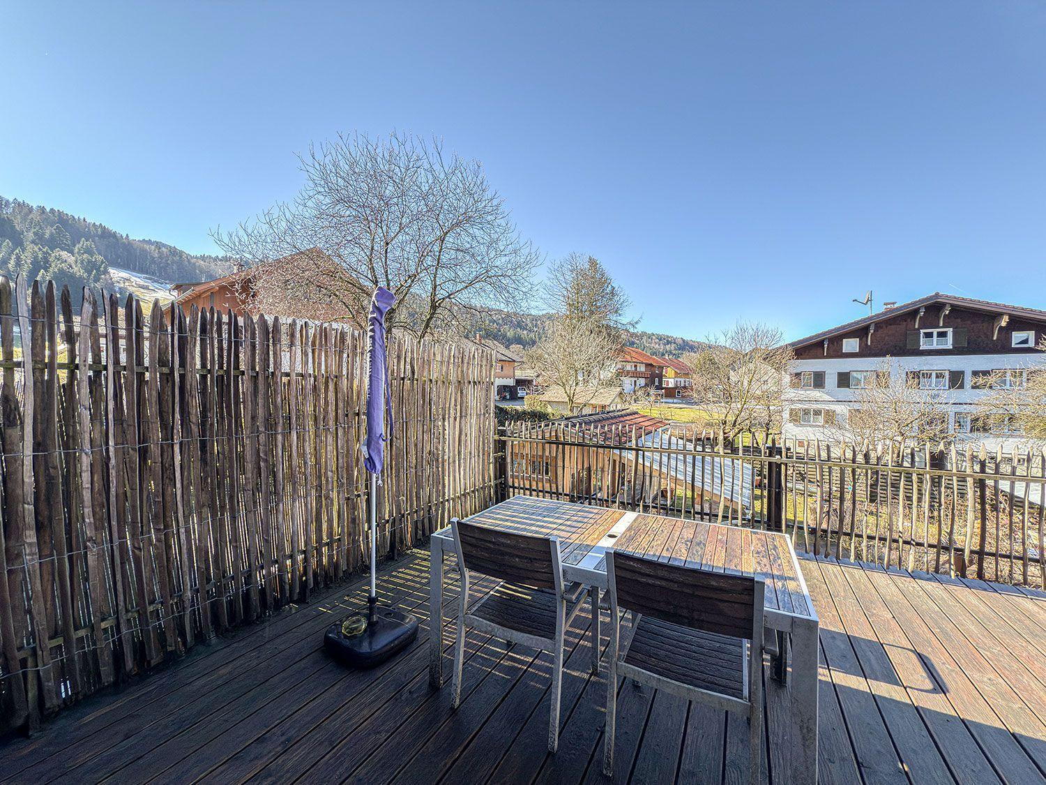 Deck with table and chairs, wooden railing, and view of the mountains.