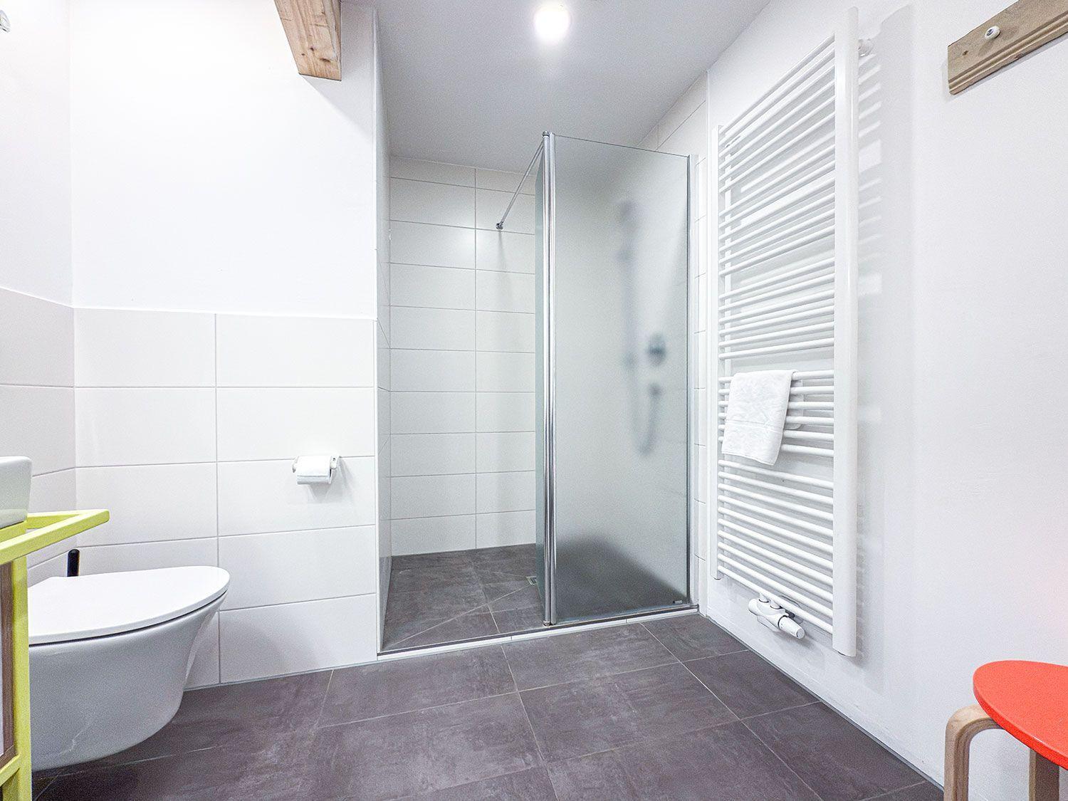 Bathroom with shower, toilet, and heater. Floor and walls are tiled.