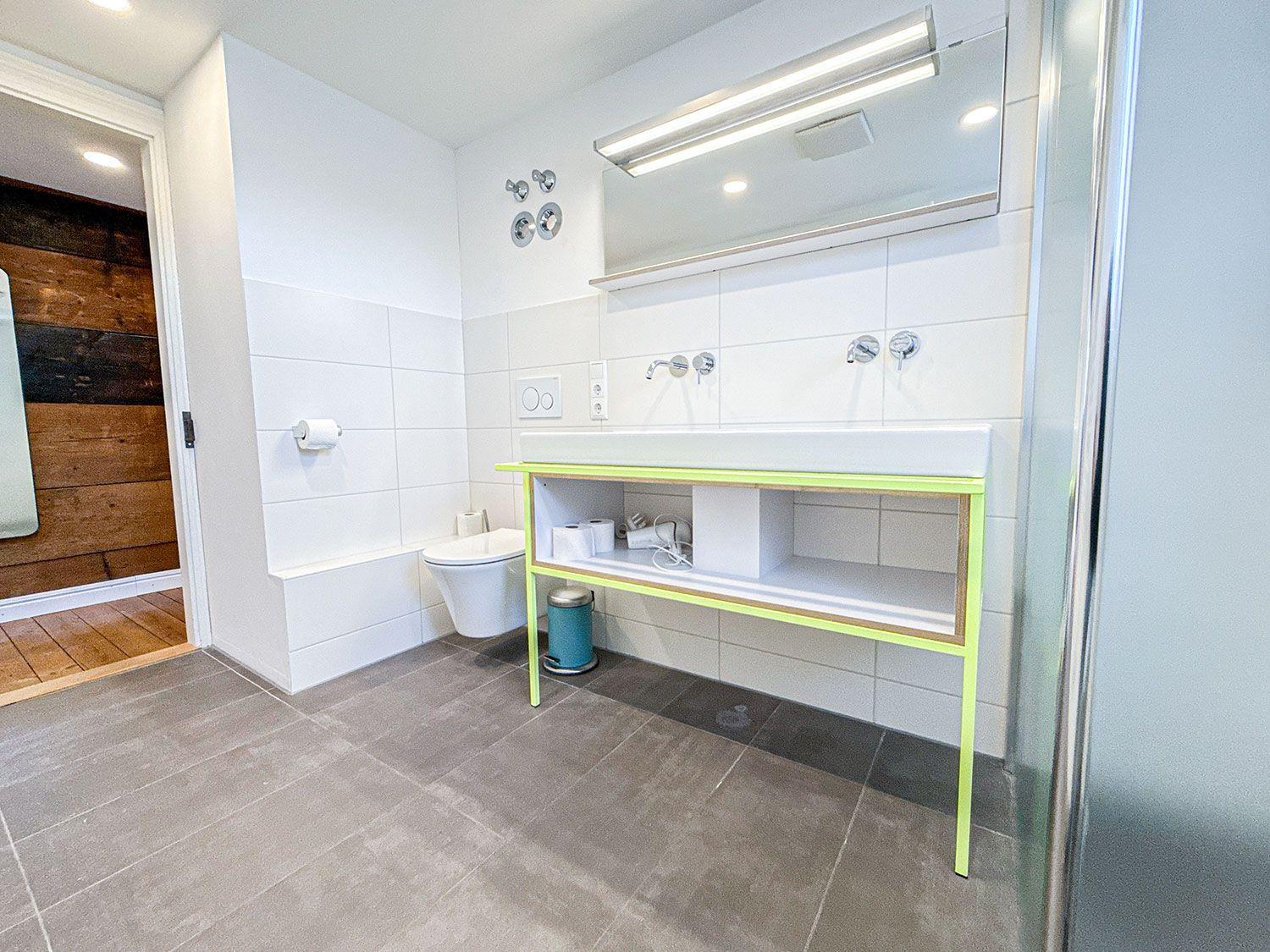 Badezimmer mit Waschbecken, Toilette und Spiegel. Gelber Waschtisch und graue Fliesen.