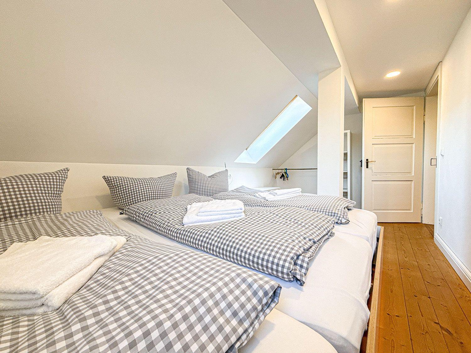 Zwei Betten mit karierten Bettwäsche unter Dachschrägen, Holzboden und Dachfenster.