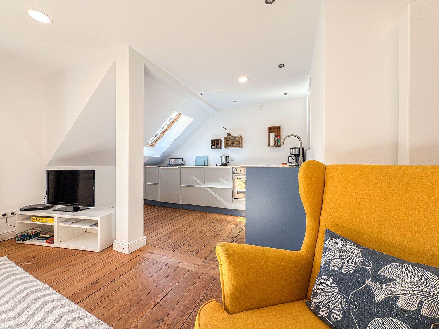 Wohn- und Küchenbereich mit gelbem Sofa, Holzboden und Dachschrägen.