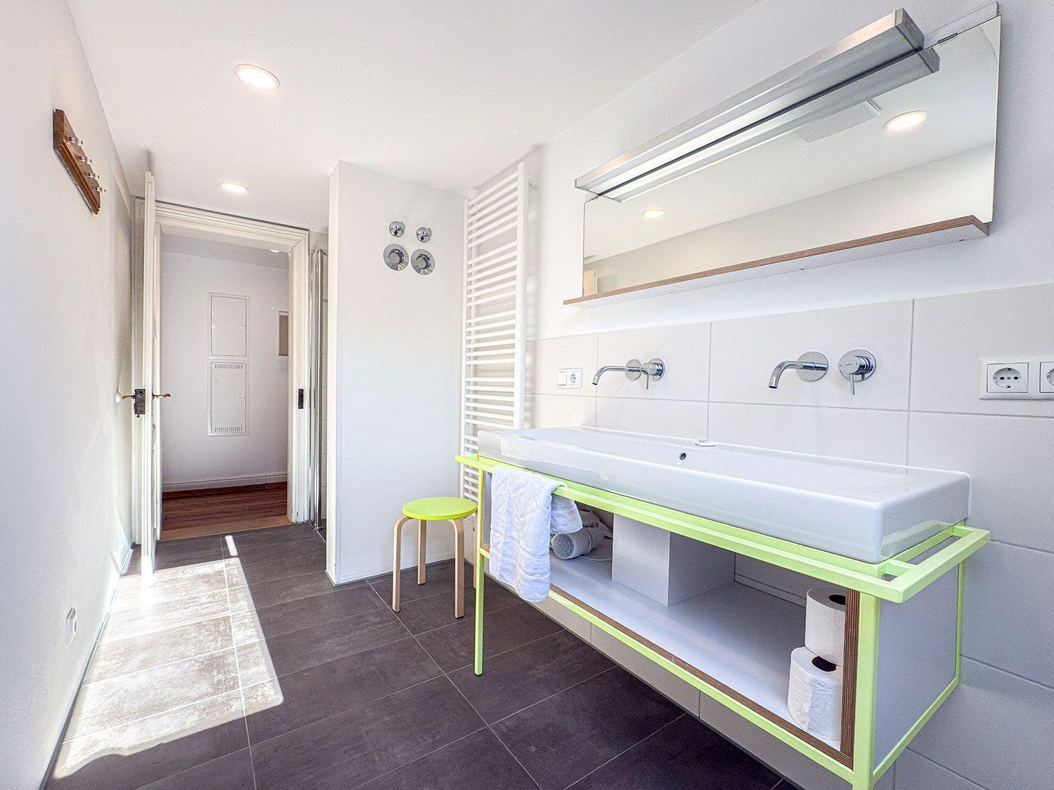 Badezimmer mit Waschbecken, Spiegel und grünem Stuhl.