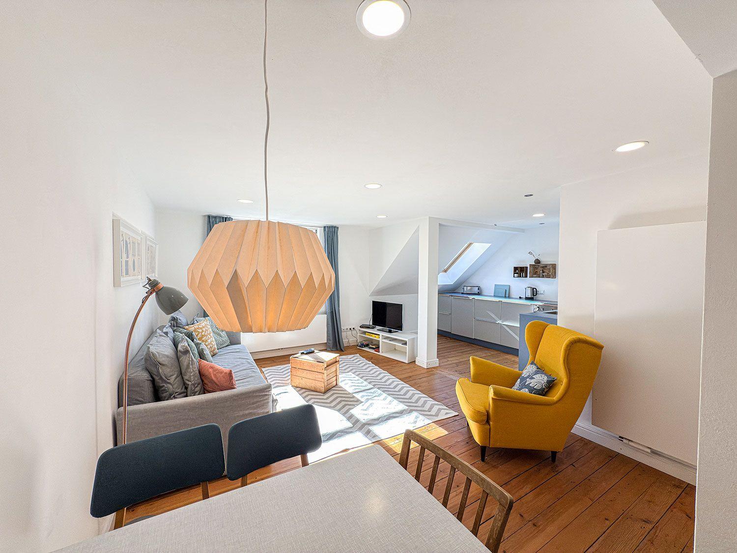 Wohnzimmer mit Sofa, gelber Sessel und Küchenbereich im Hintergrund.