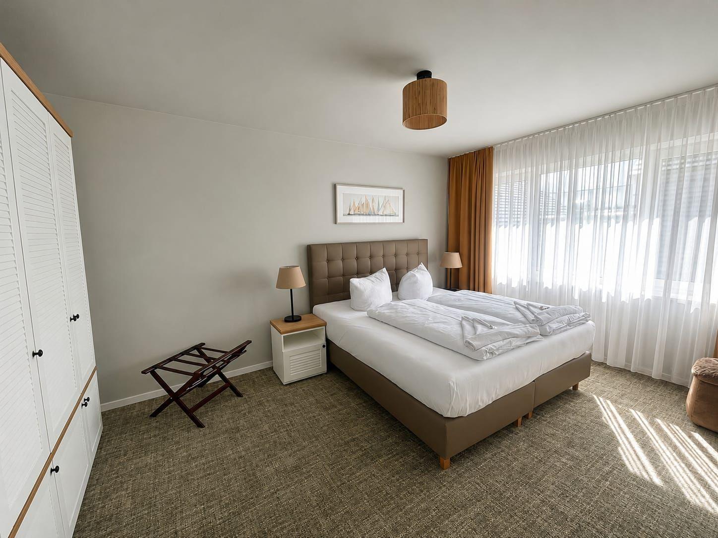 Schlafzimmer mit Doppelbett, Kleiderschrank und großem Fenster mit Vorhängen.