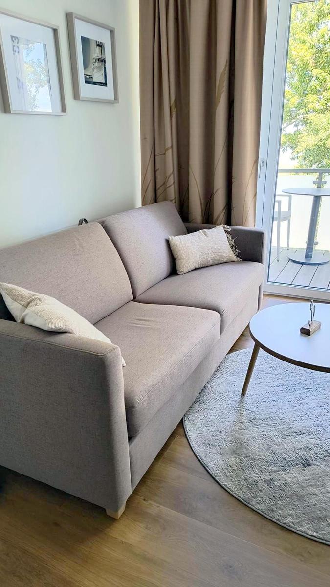 Ein grauer Sofa mit Kissen, runder Tisch und Balkon mit Blick auf Grün.