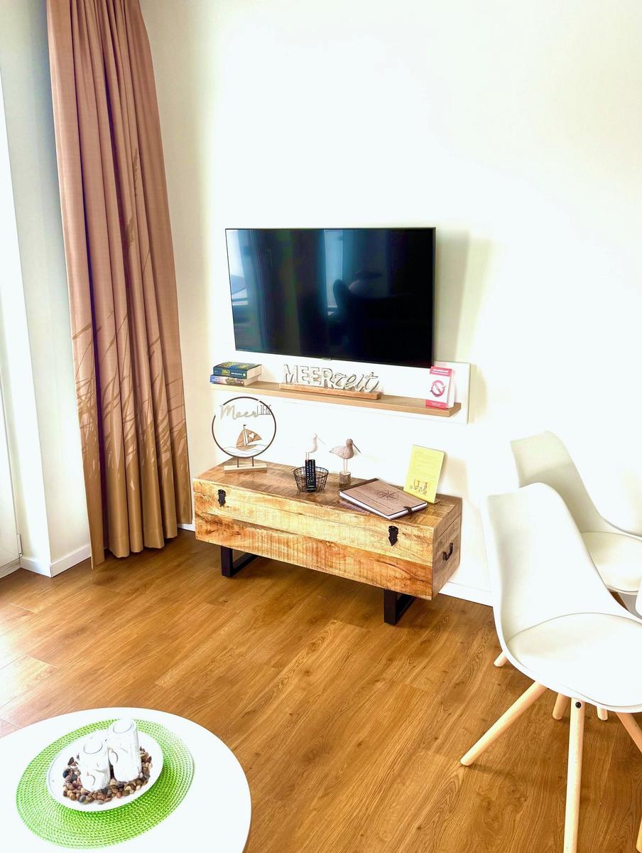 Wohnzimmer mit Fernseher, Holzkonsole und weißen Stühlen