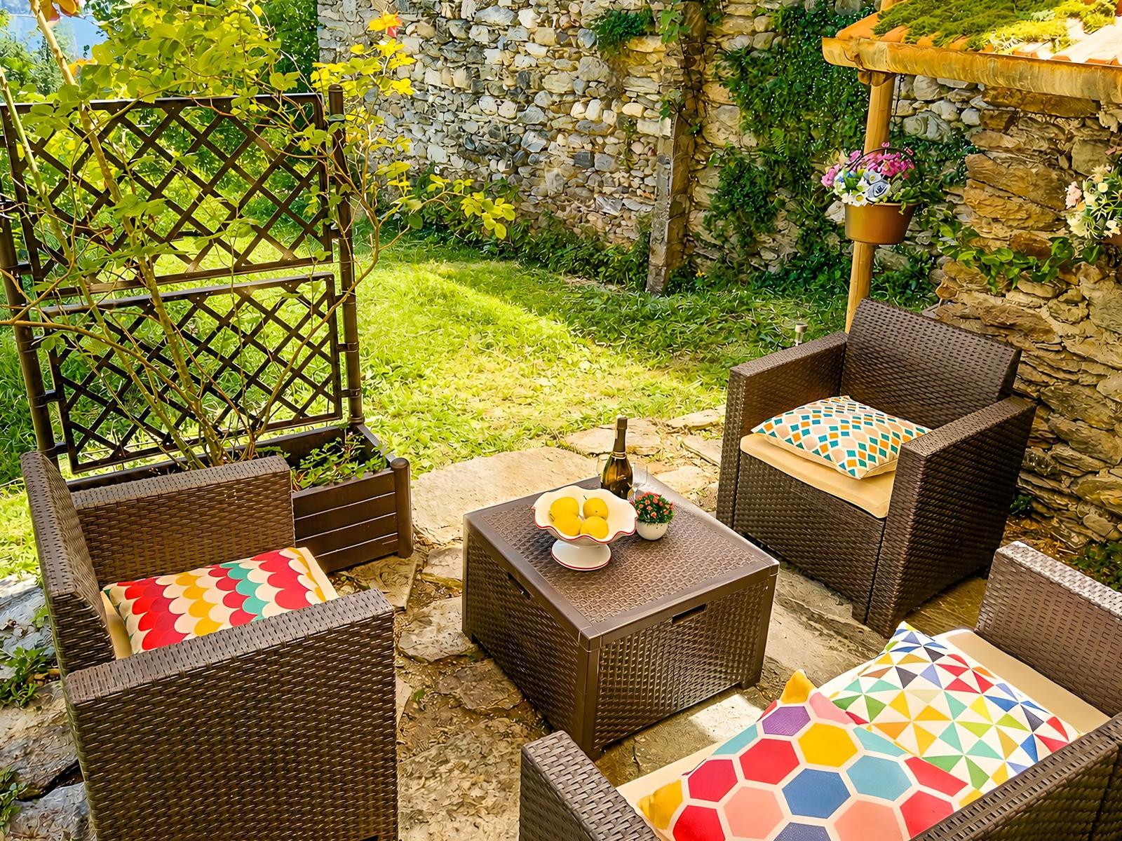 Garden area with wicker furniture, stone wall, and green lawn. Table with fruit and bottle.