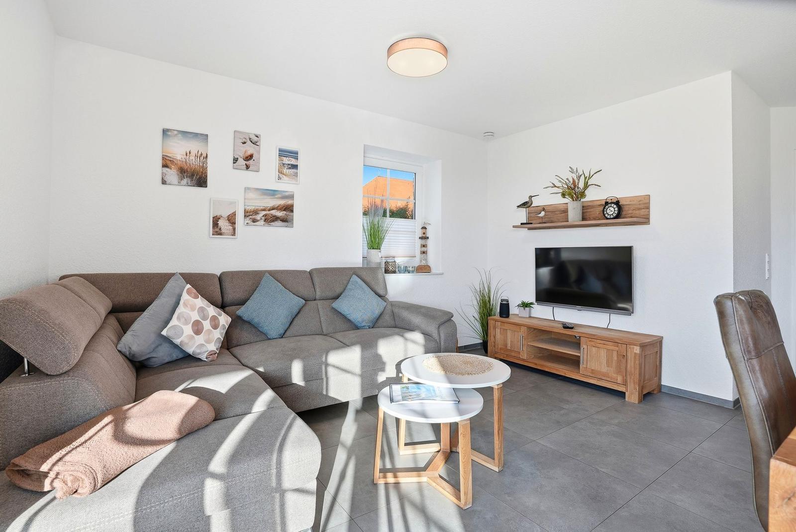 Wohnzimmer mit Ecksofa, Fernseher und Tisch. Wanddekoration und Pflanzen sichtbar.