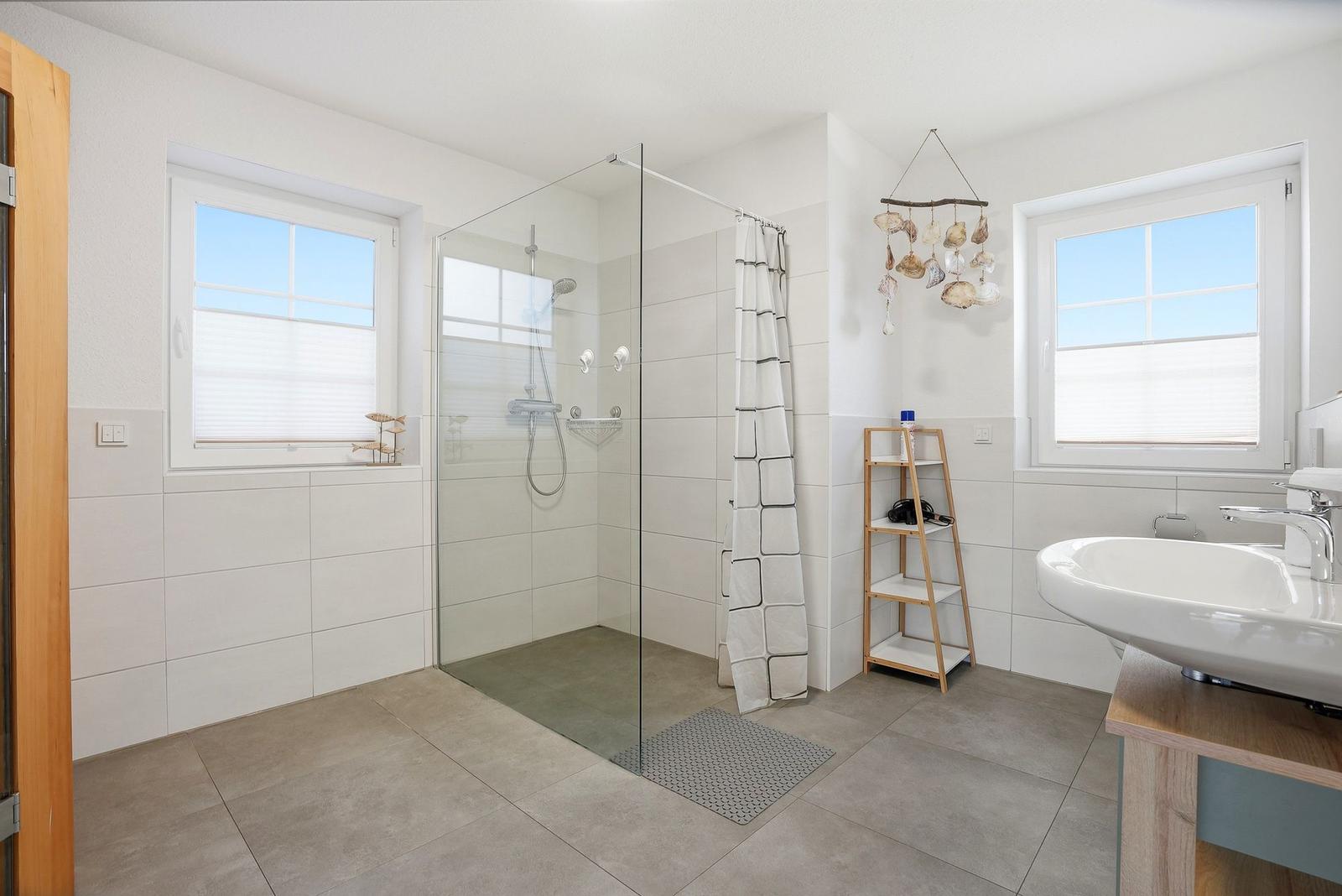 Badezimmer mit Dusche, Waschbecken und zwei Fenstern.