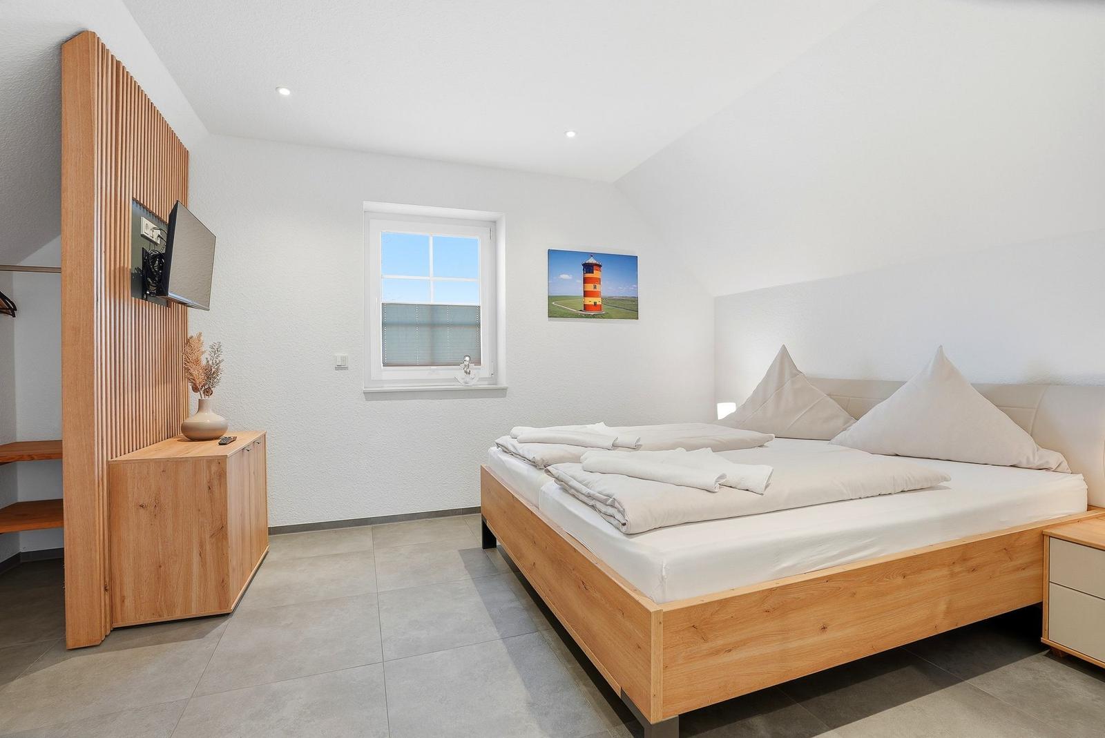 Schlafzimmer mit Holzbett, Fenster und Wandbild. Holzschrank mit Fernseher.