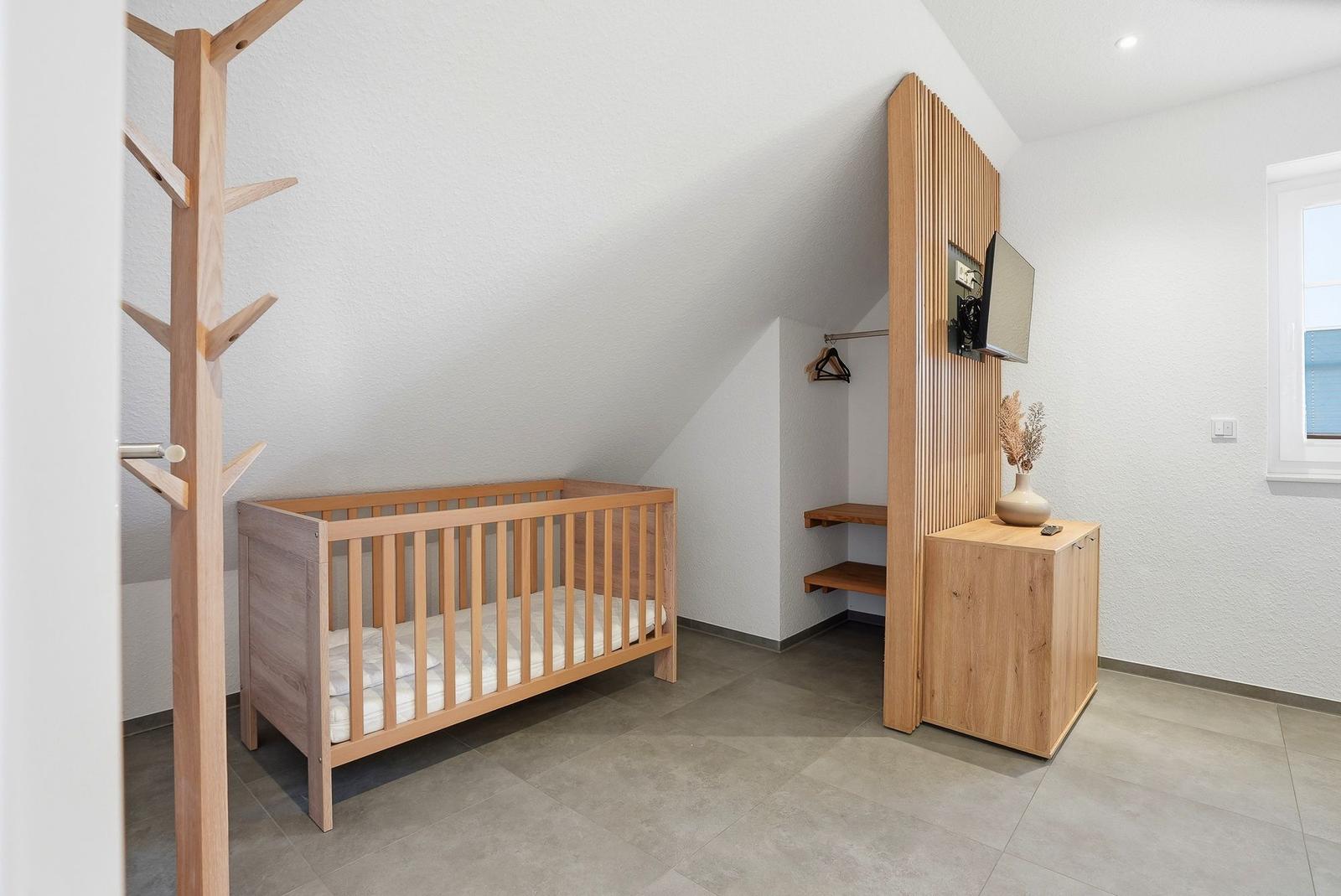 Kinderzimmer mit Holzkrippe, Kleiderständer und TV-Möbel.