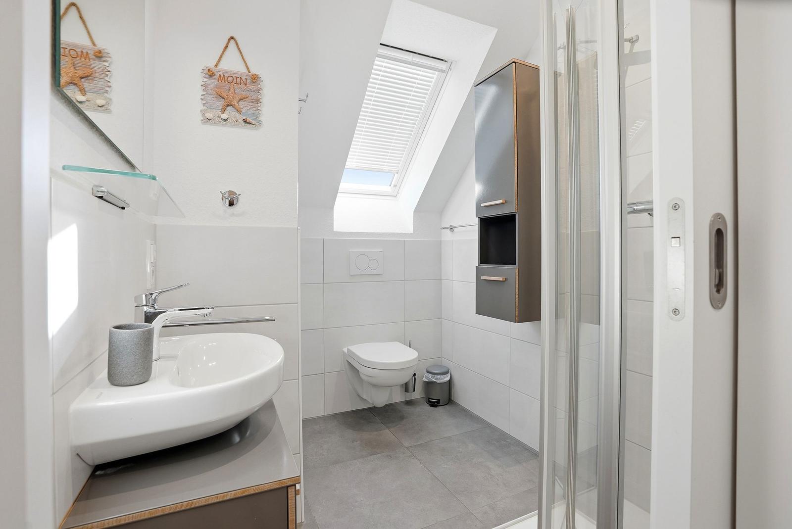 Badezimmer mit Dusche, Toilette und Waschbecken unter Dachschrägen.