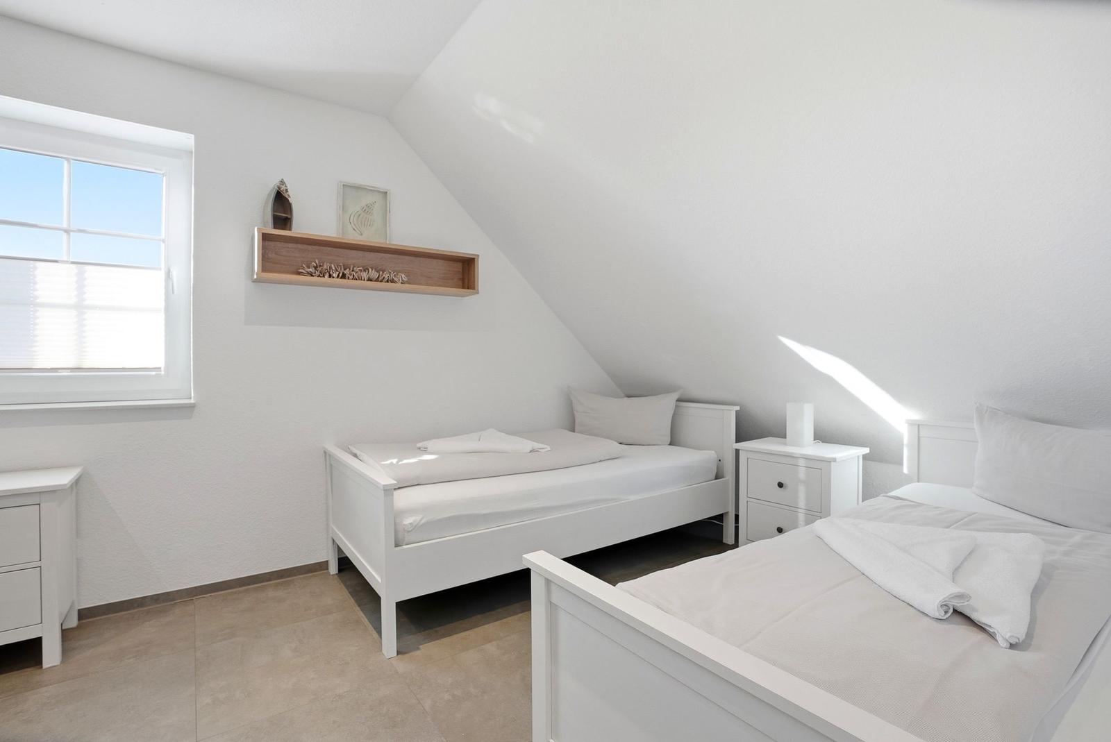Zwei weiße Einzelbetten mit Nachttischen und Fenster im Dachgeschosszimmer.