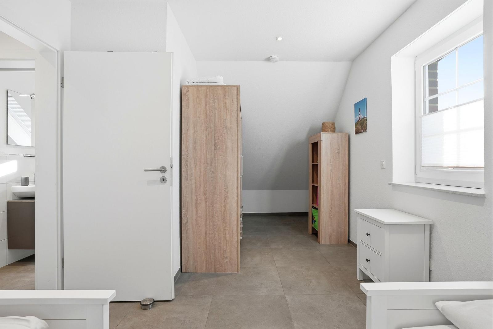 Schlafzimmer mit Kleiderschrank, Nachttisch und Fenster. Badezimmer im Anschluss.