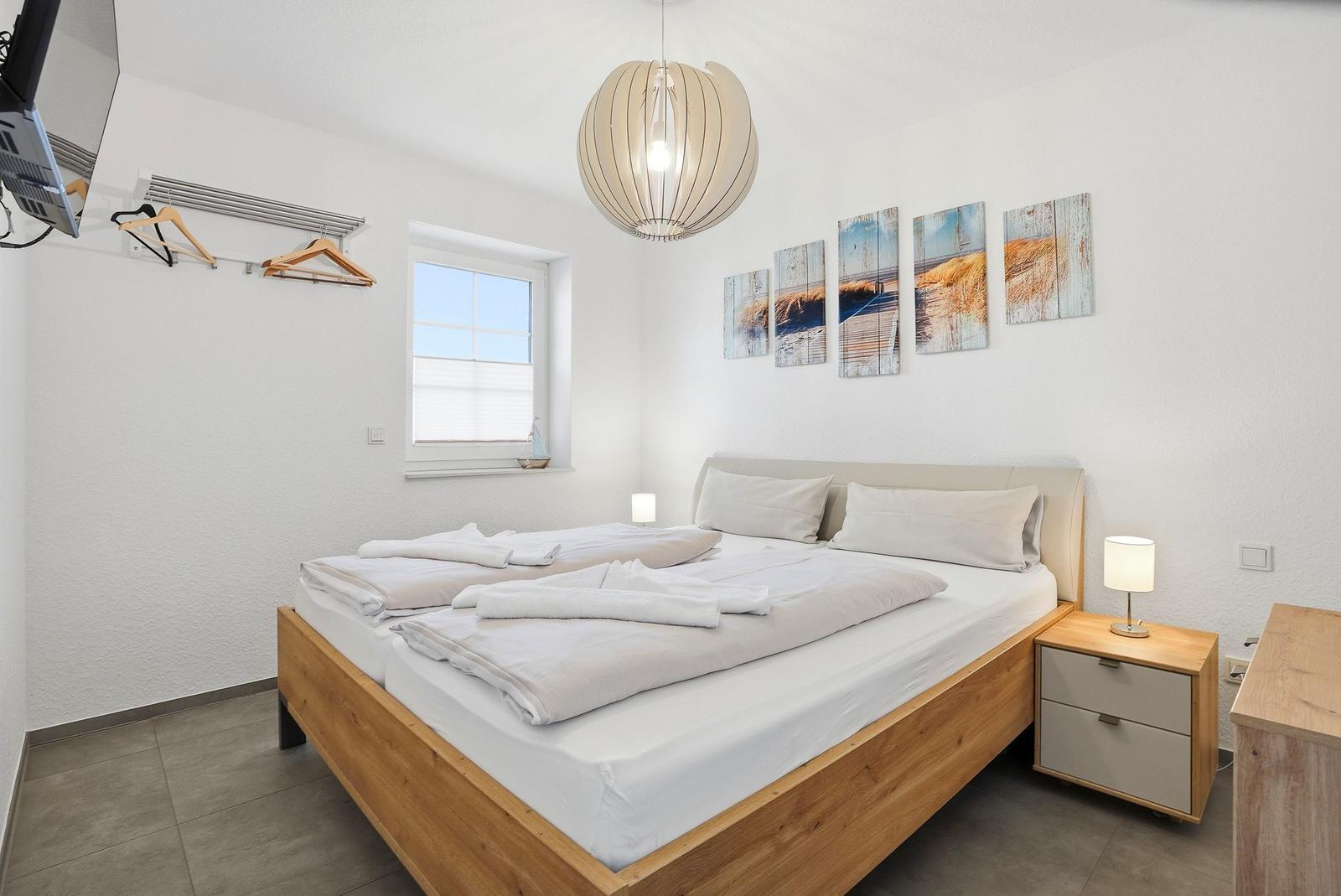Ein Schlafzimmer mit Doppelbett, Nachttisch, Wandbild und Fenster.