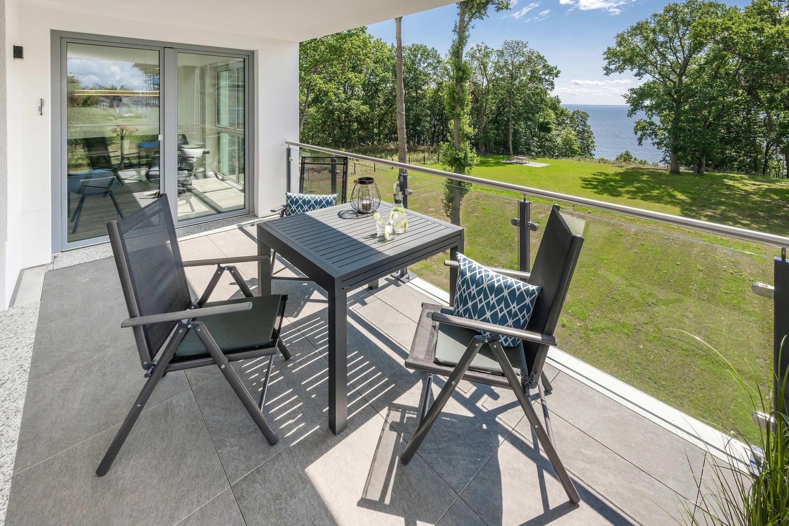 Terrasse mit Tisch und zwei Stühlen. Blick auf Grünfläche und See.