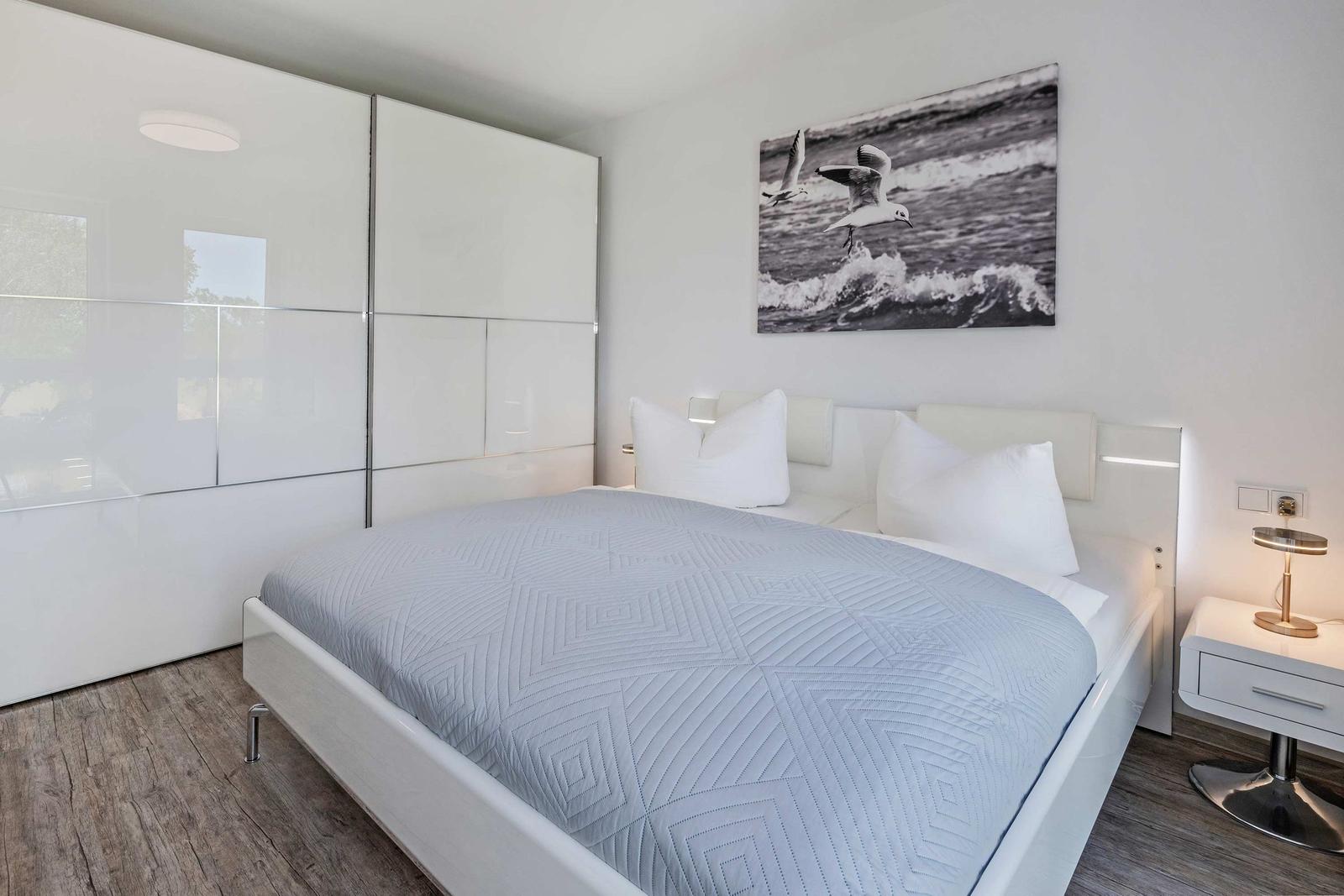 Schlafzimmer mit weißem Bett, Schwebetisch und Wandbild mit Möwen.