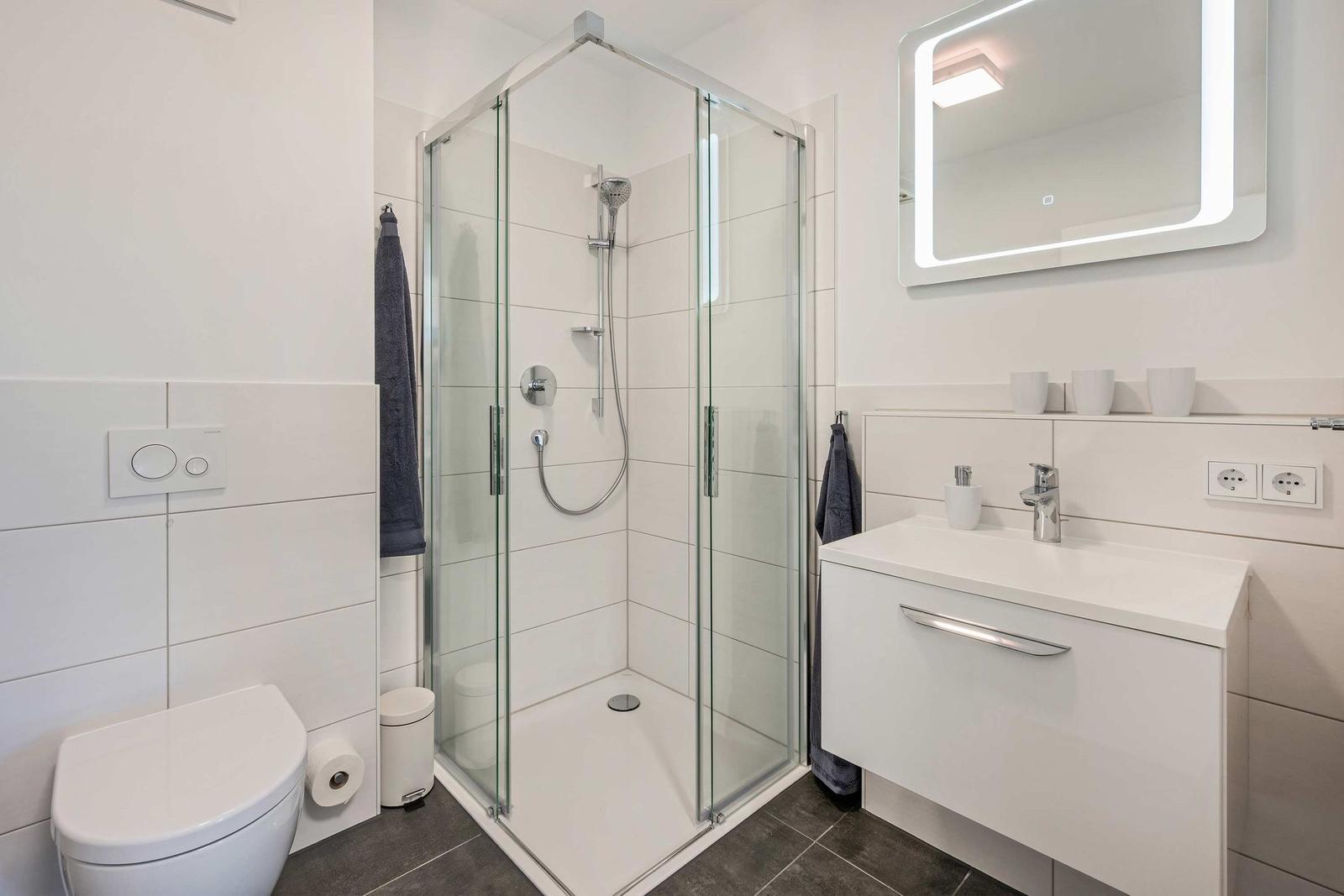 Badezimmer mit Dusche, Waschbecken und Toilette. Moderne Einrichtung mit Spiegel und Handtüchern.