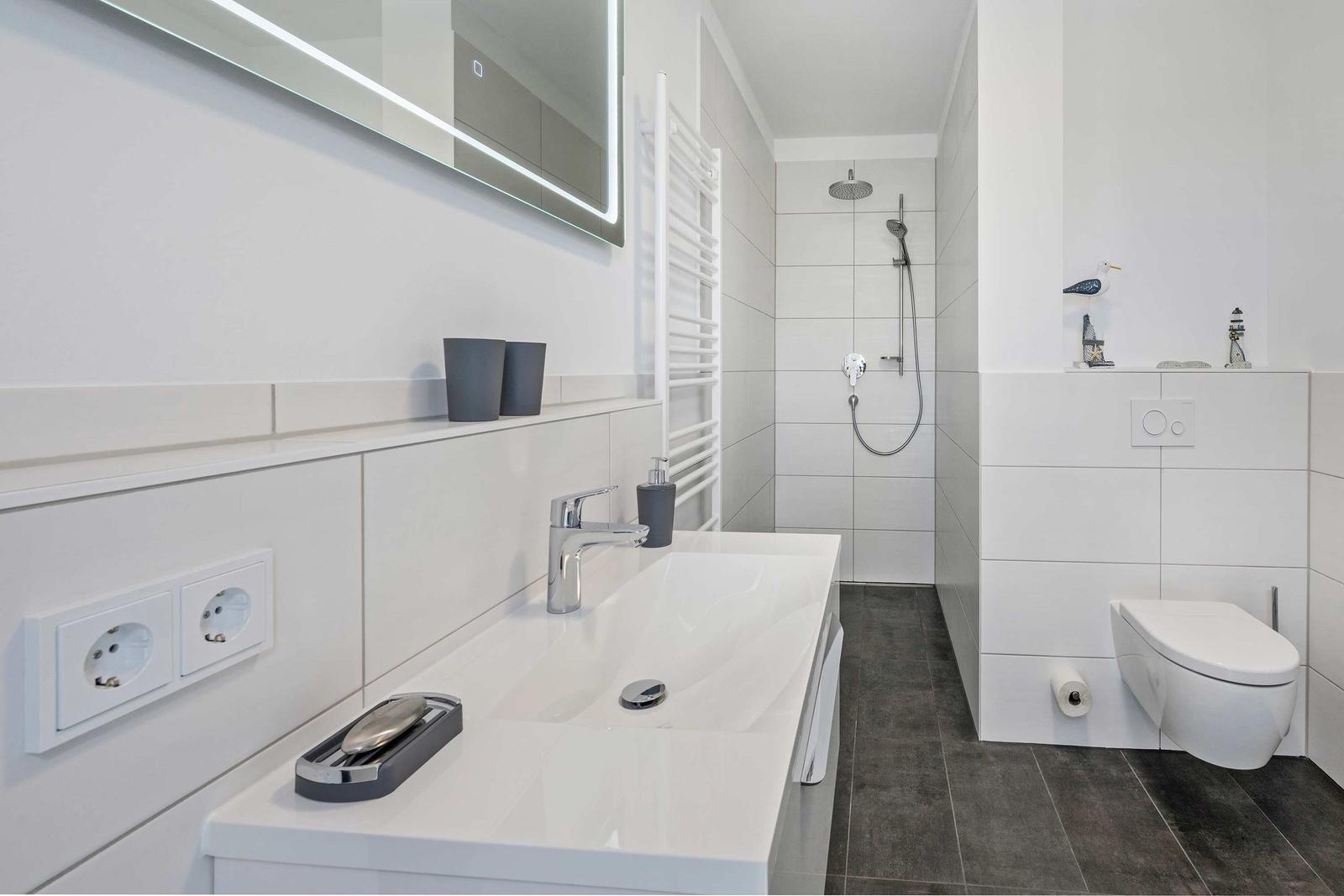 Moderne Badewanne mit Dusche, Waschbecken und Toilette. Weiße Fliesen und graue Bodenfliesen.