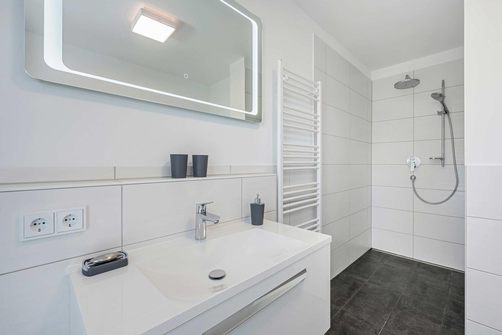 Badezimmer mit Dusche, Waschbecken und Spiegel. Fliesen und Bodenfliesen.
