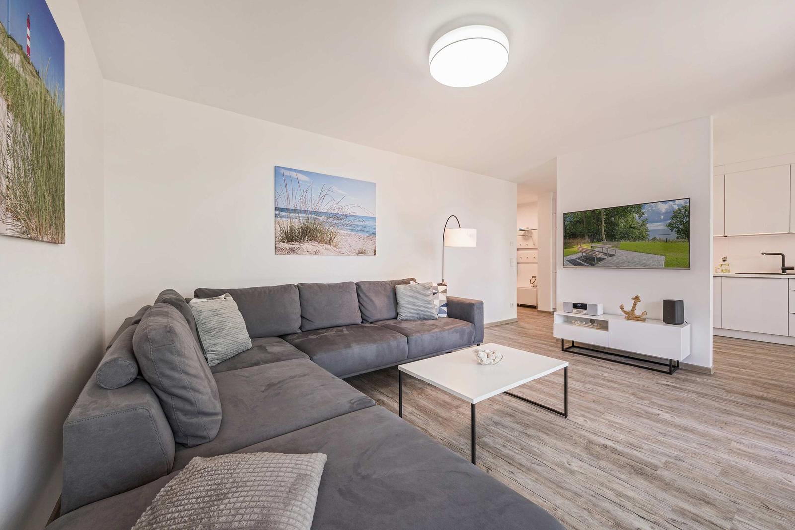 Wohnzimmer mit grauem Sofa, weißem Couchtisch und Fernseher an der Wand.
