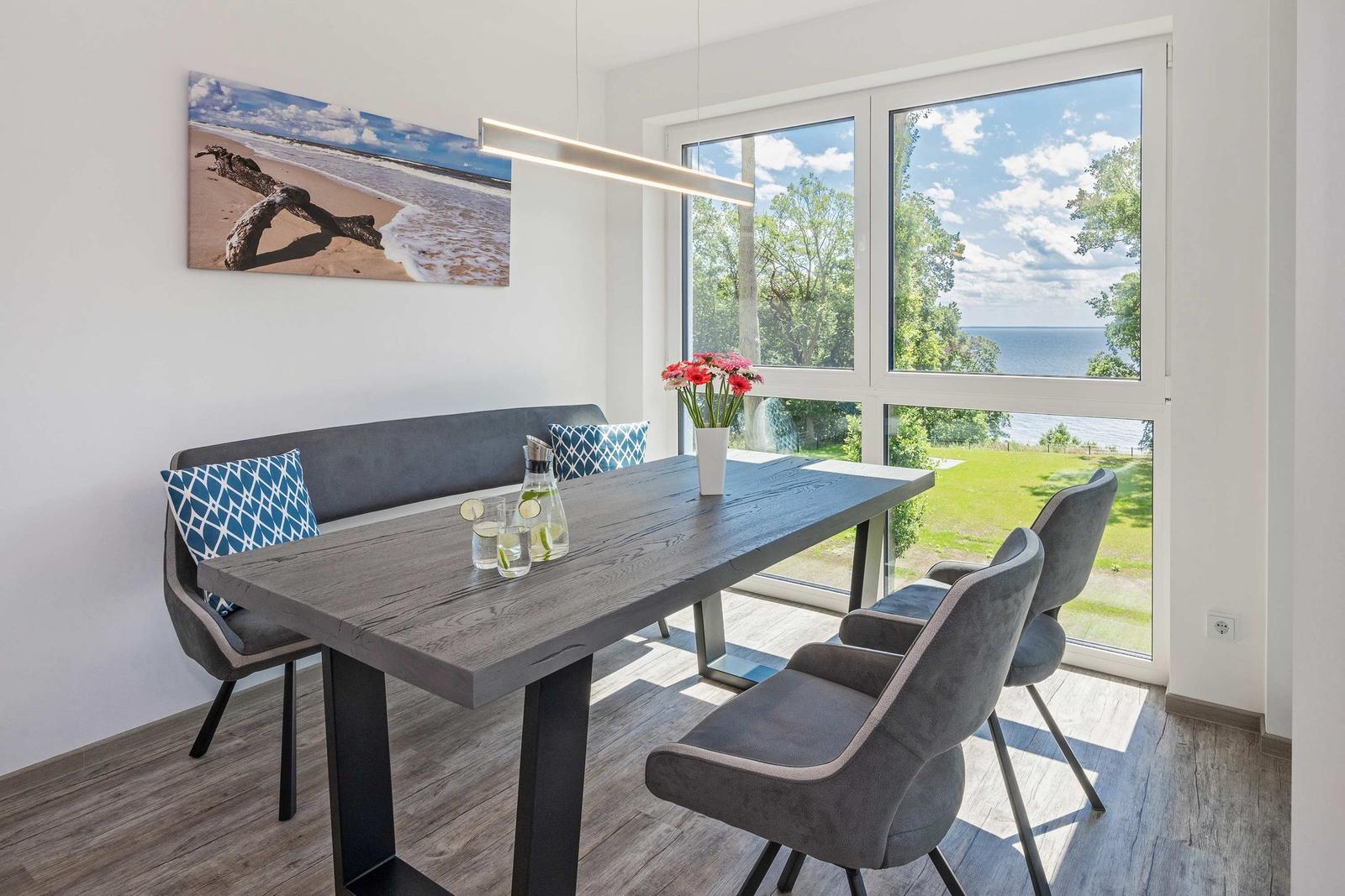 Essbereich mit Tisch, Stühlen und Blick auf Grünfläche und Meer.