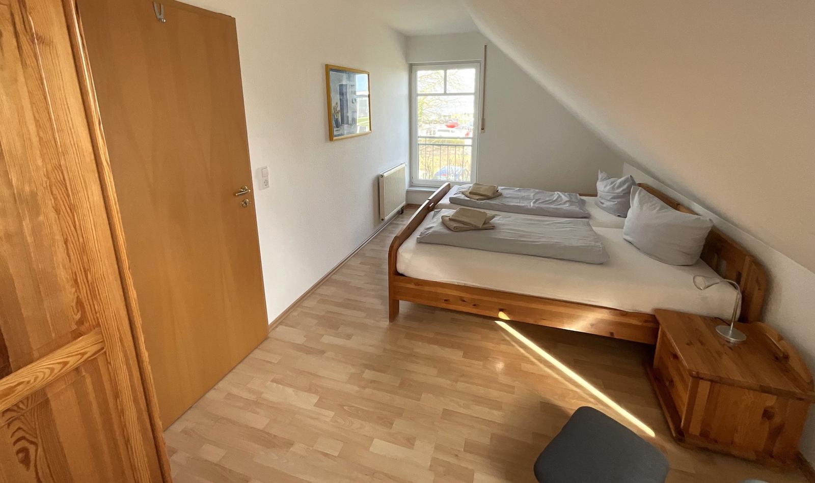 Schlafzimmer mit Holzbett, Nachttisch und Fenster mit Blick nach draußen.
