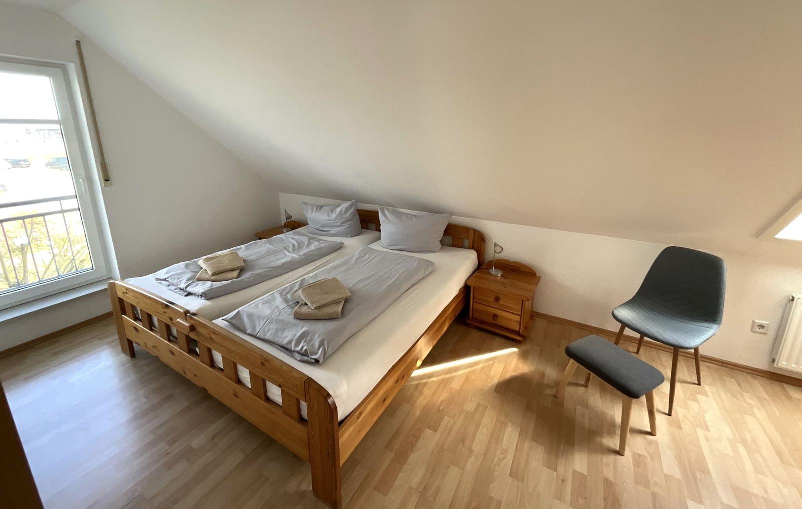 Schlafzimmer mit Doppelbett, Nachttisch und Stuhl. Holzboden und Fenster mit Blick.