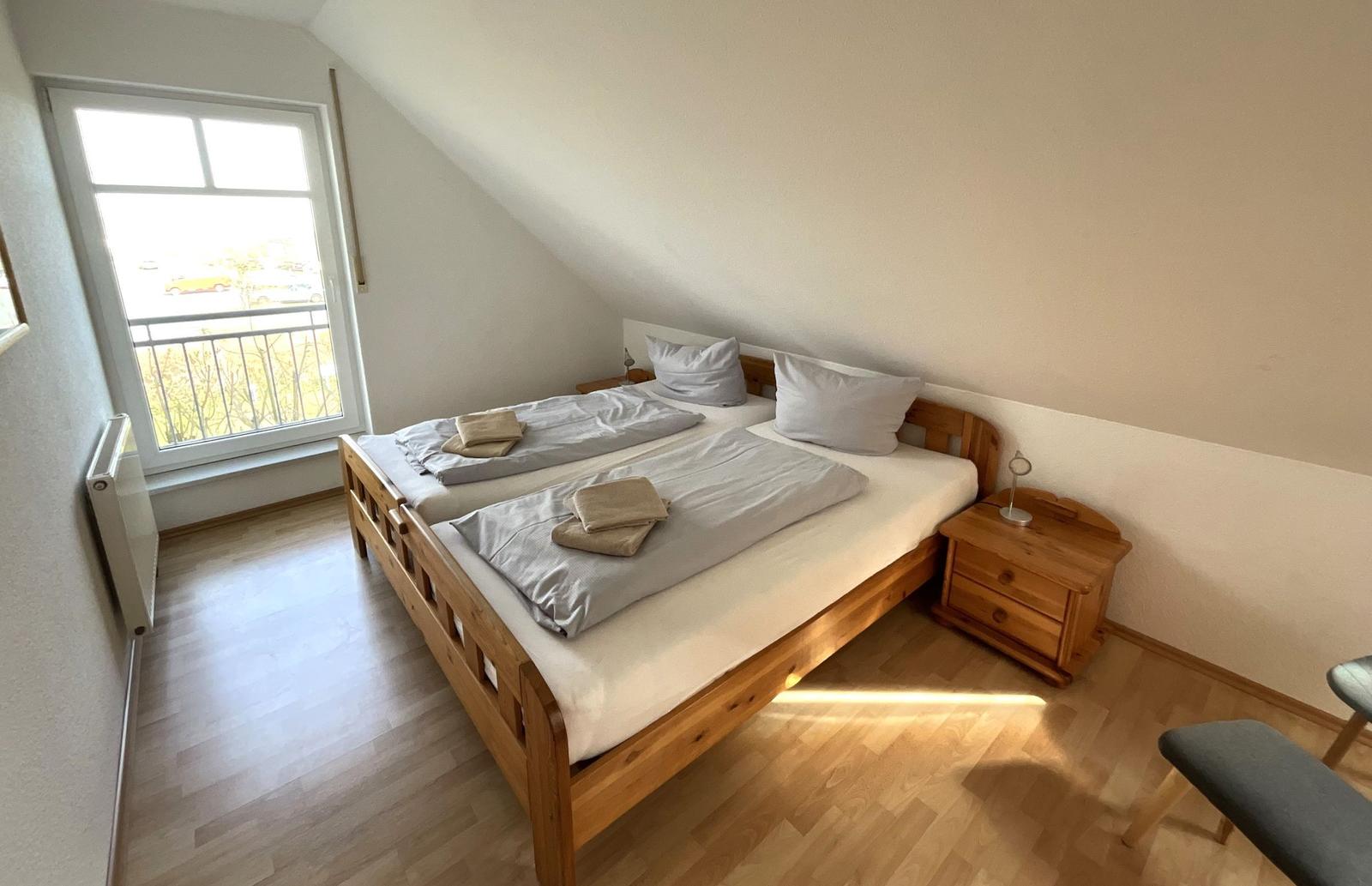 Schlafzimmer mit Doppelbett, Holzmöbel und Balkonfenster.