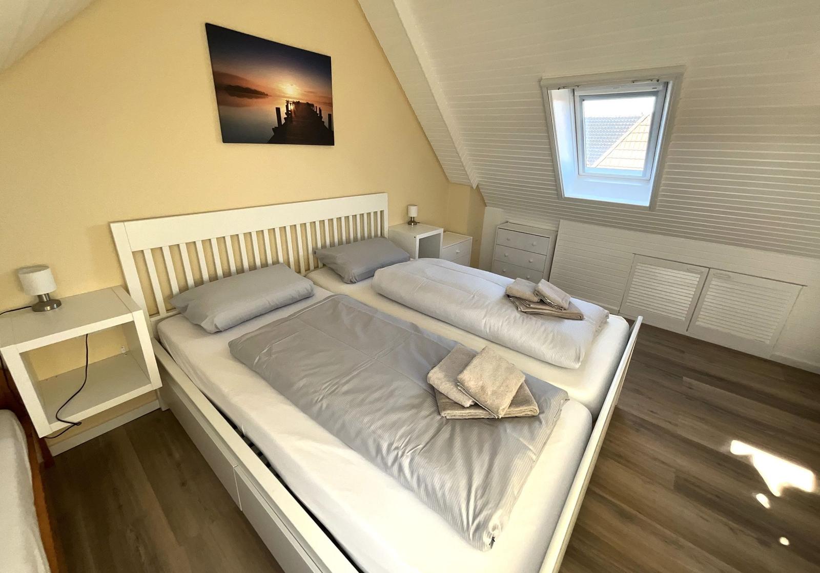 Schlafzimmer mit Doppelbett, Nachttisch und Fenster. Wandbild und Holzboden.