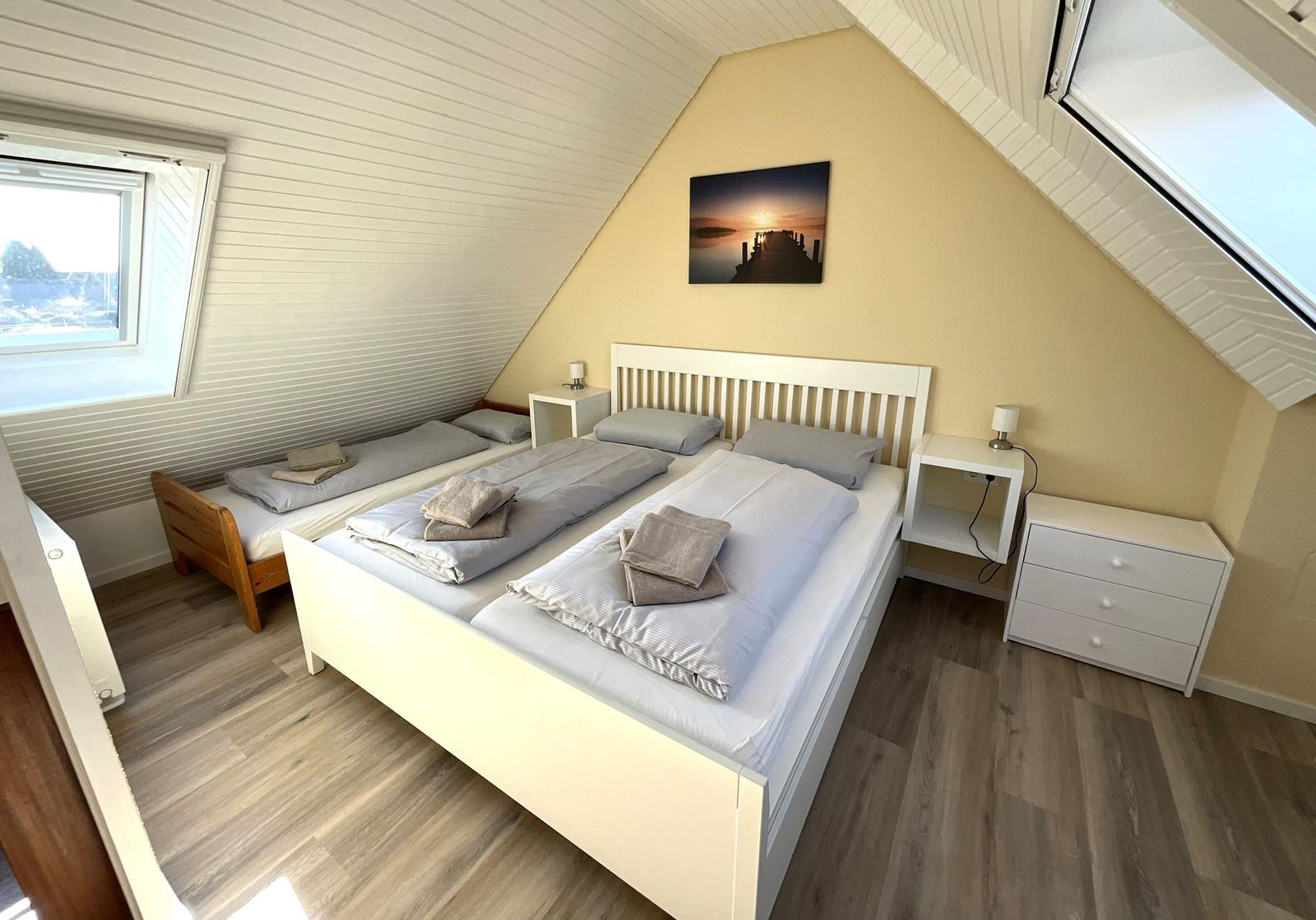 Schlafzimmer mit Doppelbett, kleinem Bett und Schreibtisch unter Dachschräge