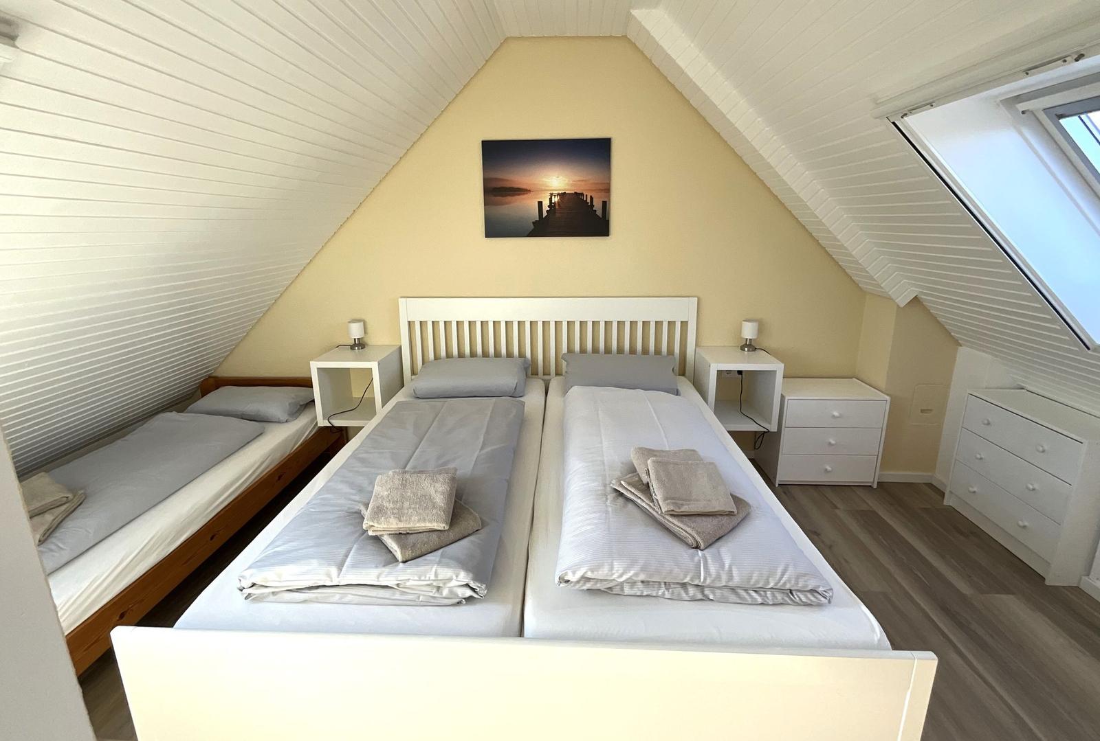 Zimmer mit zwei Betten, Schreibtisch und Fenster. Decke mit Holzverkleidung.