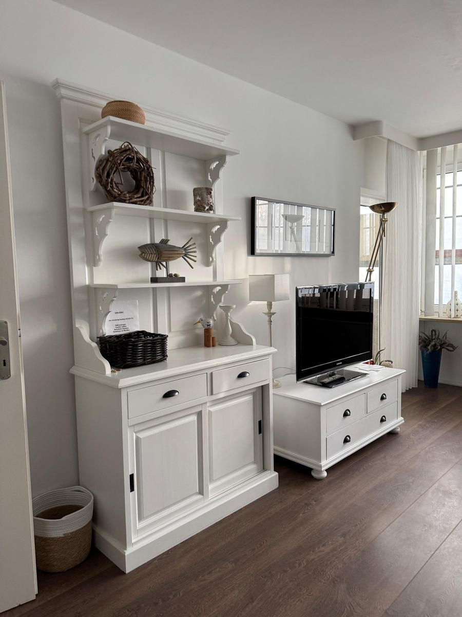 White sideboard with shelves and TV on stand. Wooden floor and window with curtains.