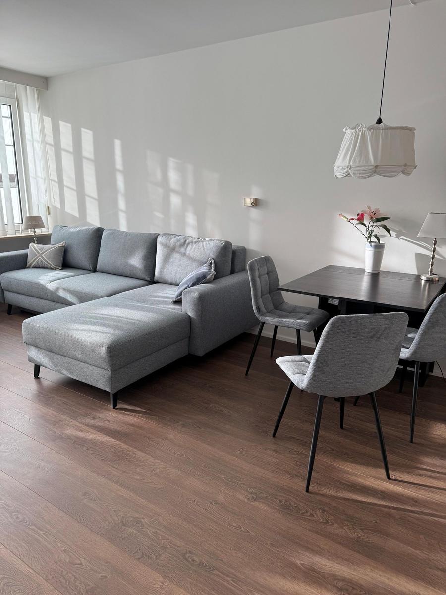 Living and dining area with gray sofa, table and chairs on wooden floor.
