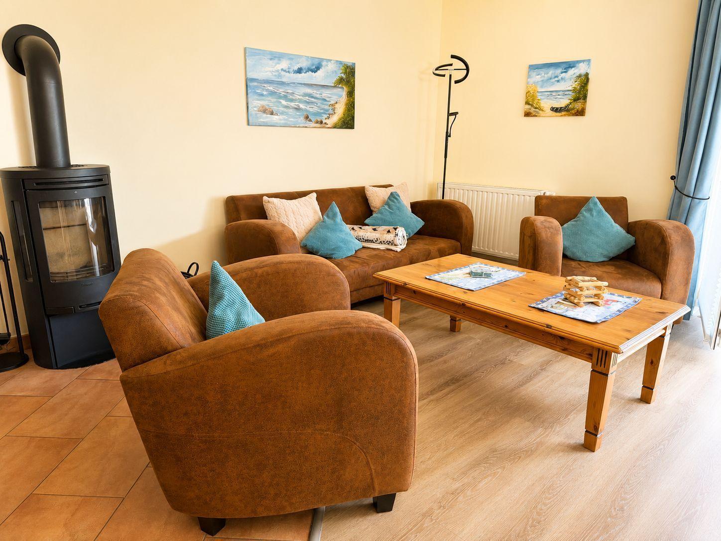 Wohnzimmer mit braunen Sitzmöbeln, Holztisch und Kaminofen an der Wand.