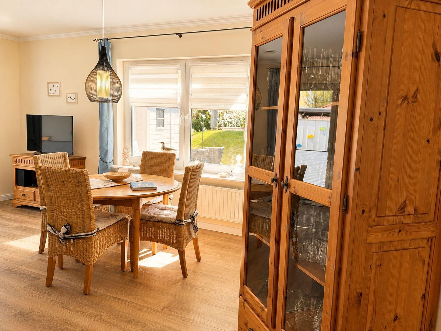 Esszimmer mit runden Tisch, Stühlen und Glasvitrine. Fenster mit Blick auf Garten.